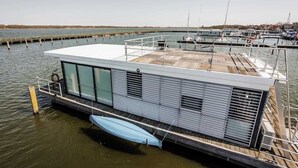 A floating house with a deck, large windows, and a covered area. - Hausboot Küstennebel 2 (Ribnitz-Damgarten)