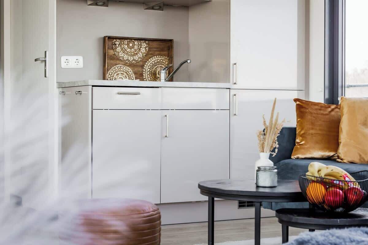 A modern kitchen with white cabinets, a black countertop, and a decorative wooden piece above the sink.