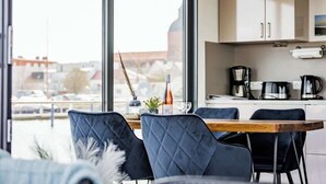 A modern kitchen with a large window, a dining table with chairs, and a coffee machine. - Hausboot Küstennebel 2 (Ribnitz-Damgarten)