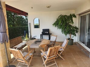 A patio with a round wooden table, four wooden chairs, a potted plant, and a grill.