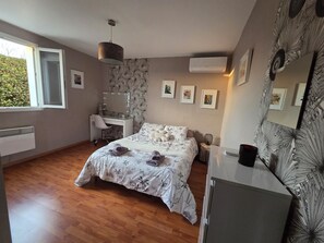 A bedroom with a bed, a desk, a chair, a dresser, a mirror, and a window.