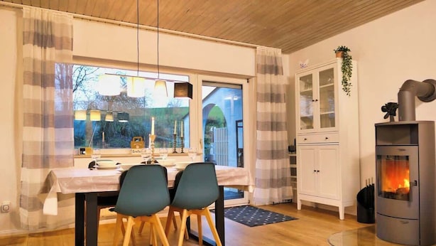 A dining area with a table set for two, a white cabinet, and a wood-burning stove. - Apfelhaus am Hennesee (Meschede)