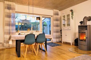A dining area with a table set for two, a white cabinet, and a wood-burning stove. - Apfelhaus am Hennesee (Meschede)