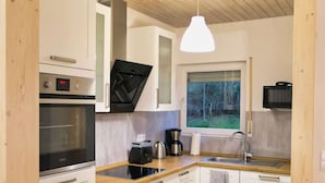 A compact kitchen with white cabinets, a built-in oven, a microwave, and a coffee maker. There's a window providing a view of the outdoors. - Apfelhaus am Hennesee (Meschede)