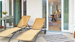 Een modern buiten zitgedeelte met twee wicker lounge fauteuils, een kleine tafel met een bloevas en een glazen deur naar een eetruimte.