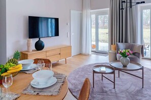 Un salon moderne doté d’un téléviseur à écran plat, de meubles en bois, d’une table à manger dressée avec des assiettes et des verres, et offrant une vue sur l’extérieur.