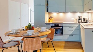 Een moderne keuken met lichtblauwe kastjes, een eethoek met rieten stoelen en een koffieapparaat.