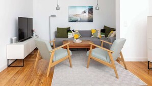 Una sala moderna con un sofá, dos sillones, una mesa de centro y un televisor sobre un mueble.