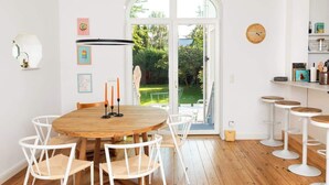 Un comedor con una mesa redonda de madera, sillas blancas y un ventanal de vidrio que da a un jardín.