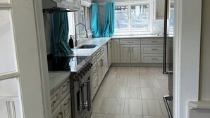 Een moderne keuken met witte kastjes, een roestvrijstalen fornuis en een raam met gordijnen.