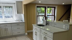 Een moderne keuken met witte kastjes, een marmeren aanrechtblad en een groot raam dat voor natuurlijk licht zorgt.