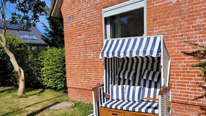Ein Liegestuhl mit gestreiftem Sonnendach, eine Ziegelwand und ein Fenster.