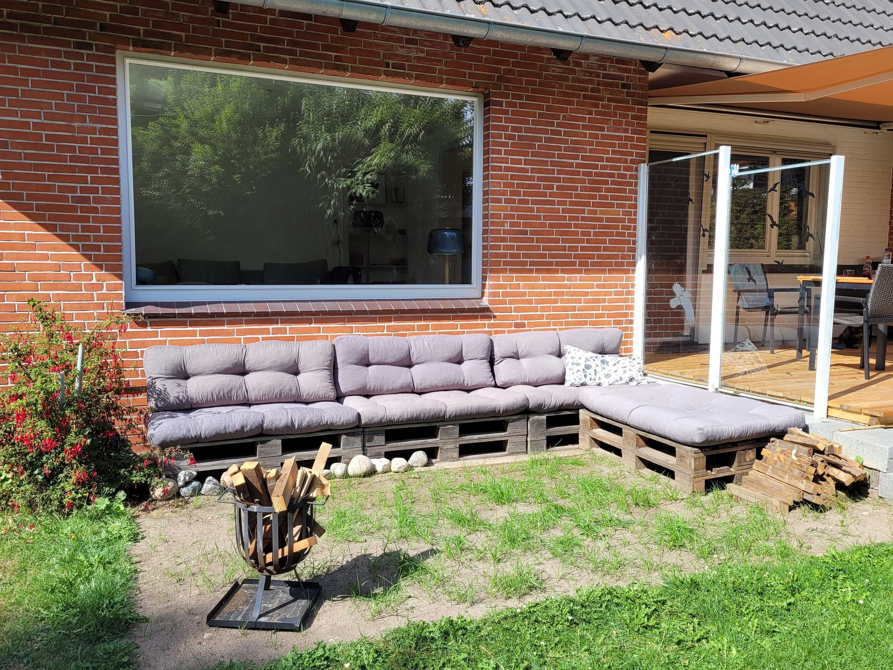 A brick house with a large window, a wooden bench, and a fire pit.