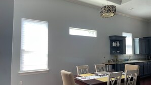 Un comedor con una mesa y sillas de madera, una araña y una cocina al fondo.