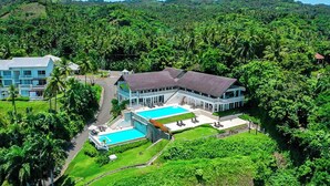 Un resort con una piscina grande, varias habitaciones y exuberante vegetación tropical.