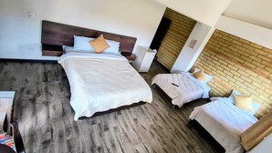 Een hotelkamer met een groot bed, twee kleinere bedden, een houten vloer, een bakstenen muur en een wit plafond.