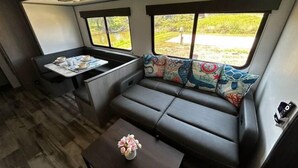 Een compact camperinterieur met een bank, een eettafeltje en een raam met uitzicht op groen.