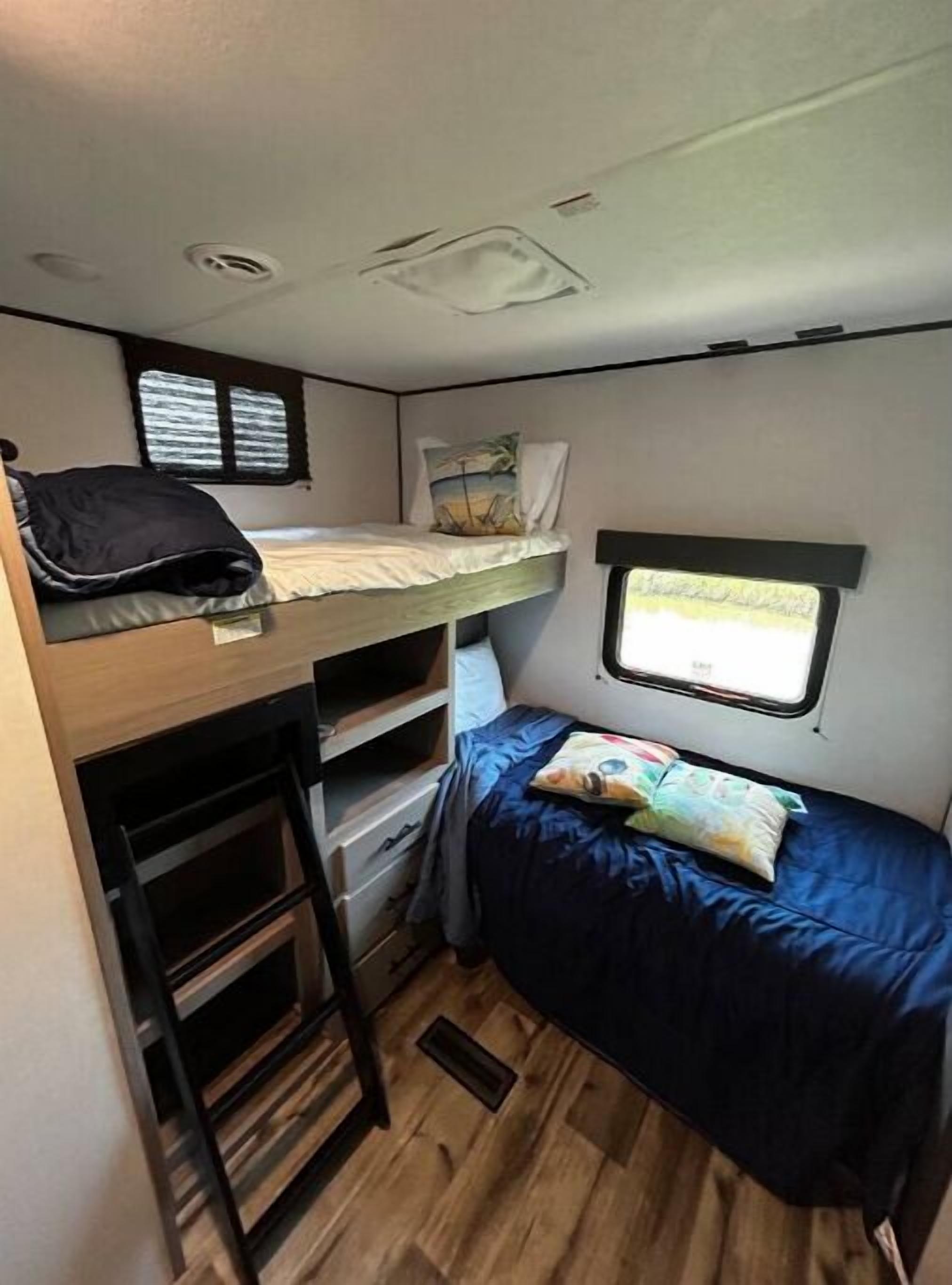 Indretning i en kompakt autocamper med køjeseng, lille tekøkken og et vindue med udsigt til naturen.