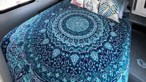 Een compact slaapkamer in een camper met een bed, een raam en een dakventilator.
