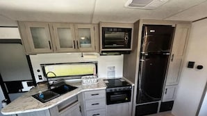 Een ruimtelijk RV-keuken met een spoelbak, fornuis, magnetron en koelkast.