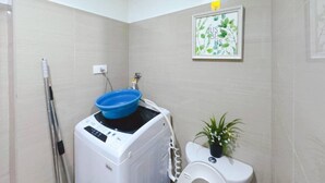 Ein kleines Badezimmer mit Waschmaschine, Toilette und einem Wandregal mit einem Bilderrahmen.