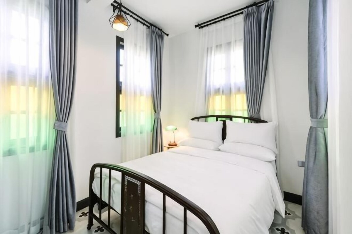 A bedroom with a bed, curtains, a bedside lamp, and a window.