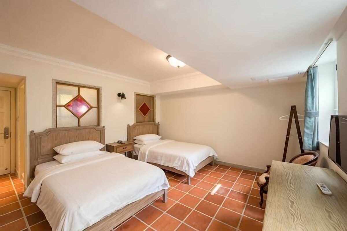 A hotel room with two beds, a desk, a chair, and a window.