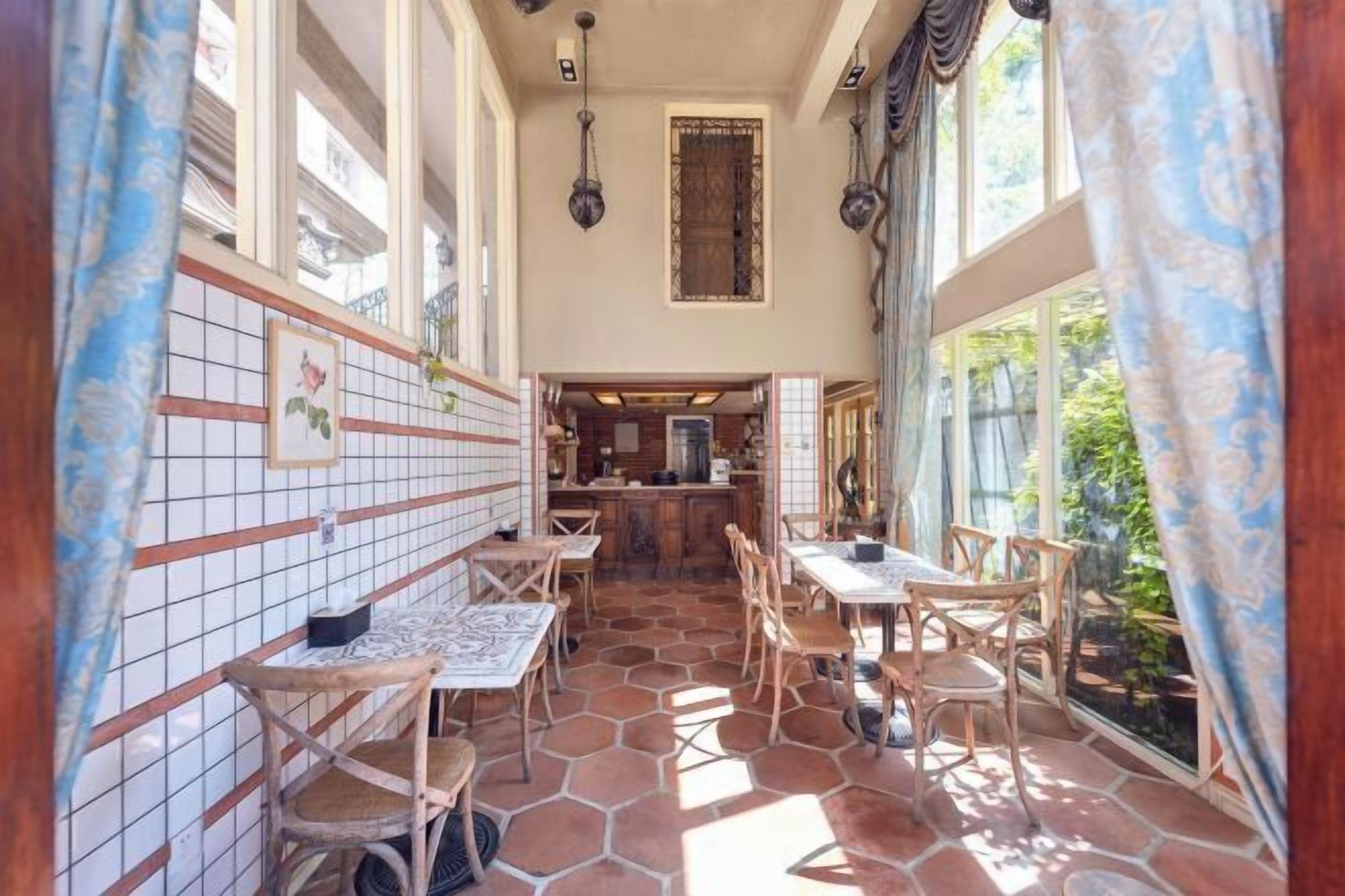 A sunlit interior with tiled walls, wooden furniture, and a view through large windows.