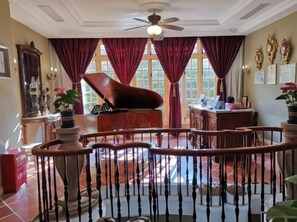 Una sala amplia con un piano, barandal de madera y ventilador de techo.