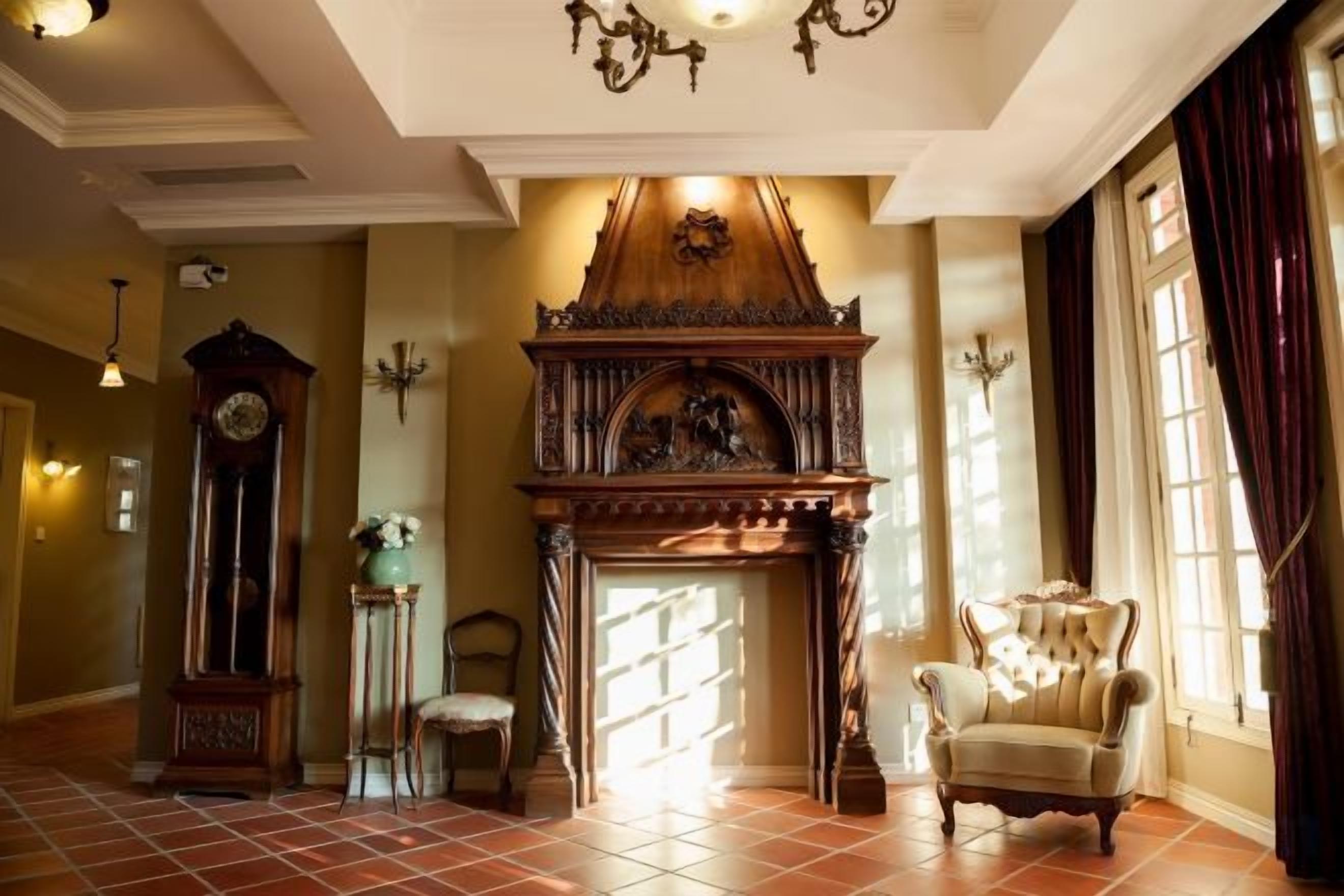 A room with a fireplace, a clock, a chair, and a large window.