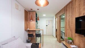 Una sala moderna con un sofá, una mesa de centro y un televisor. Se observa una pared de madera y una puerta al fondo.