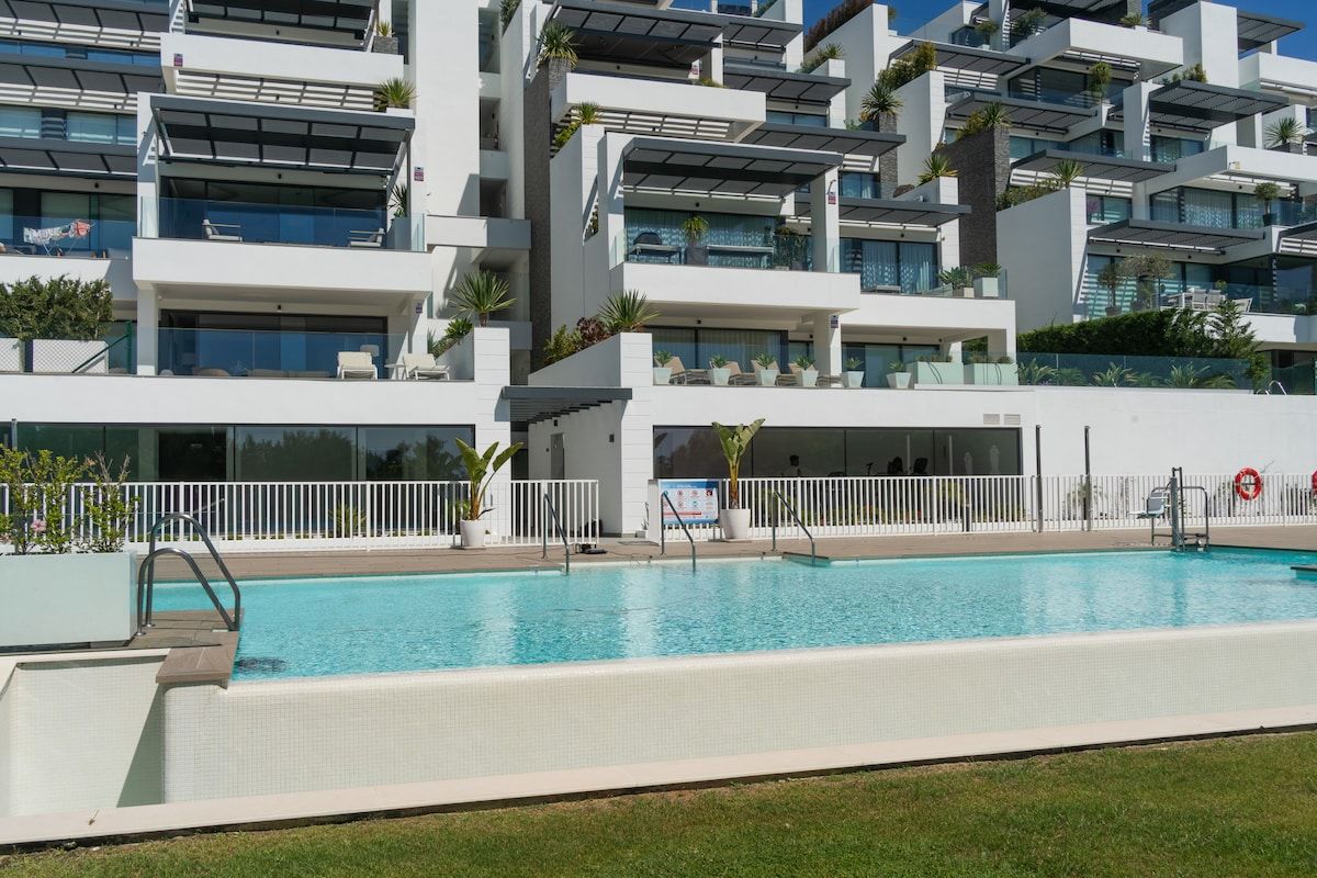 A modern building with a swimming pool, balconies, and outdoor seating areas.