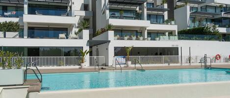 A modern building with a swimming pool, balconies, and outdoor seating areas.