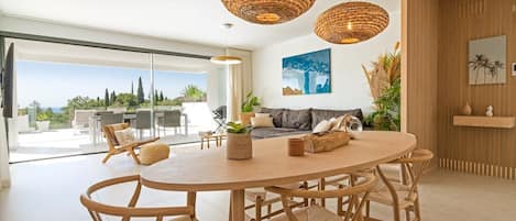 A modern dining area with a round wooden table, wicker chairs, and two hanging wicker lamps.