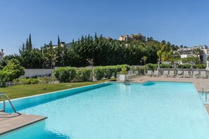 A swimming pool with a wooden deck, surrounded by greenery and a white fence. - Aqualina de Madeira (Benahavís)