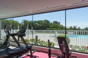Un gimnasio con equipo de ejercicio y vistas a una piscina a través de amplios ventanales.
