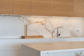 A kitchen with wooden cabinets, a marble countertop, and a modern faucet. - Aqualina de Madeira (Benahavís)