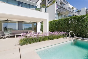 A modern outdoor pool area with a glass-enclosed seating area and a lush flower bed. - Aqualina de Madeira (Benahavís)