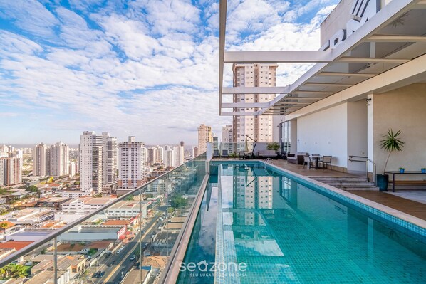 A rooftop infinity pool with a city view, modern architecture, and outdoor seating.