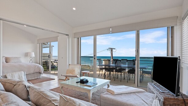 Une chambre d’hôtel moderne dotée d’un grand balcon, d’une table basse en verre et offrant une vue sur la plage et l’océan.