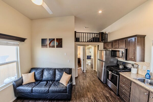 A modern kitchen with stainless steel appliances, a black leather sofa, and a staircase leading to an upper level.