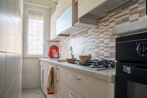 Une cuisine équipée d’une cuisinière à gaz, d’un évier et d’une fenêtre avec un rideau.