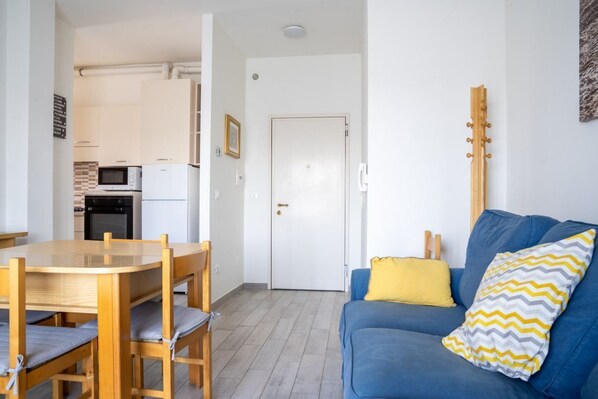 Un espace de vie compact comprenant un coin repas, une kitchenette, un canapé agrémenté de coussins à motifs et une guitare appuyée contre le mur.