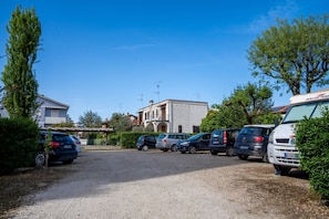 Un espace de stationnement avec plusieurs voitures, un bâtiment doté d’un balcon et un ciel bleu dégagé.