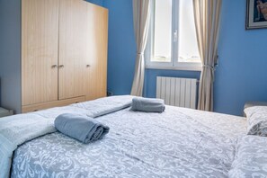 Une chambre à coucher avec un lit, une armoire, une fenêtre avec des rideaux et un radiateur.