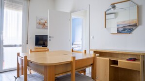 Een kamer met een houten eettafel, stoelen, een televisie, een spiegel en een klein schap.