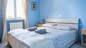 Een slaapkamer met een bed, gordijnen, een nachtkastje, een lamp en een foto aan de muur.