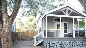 A single-story house with a porch, a stone foundation, and a wooden fence in the background. - Moab Tiny Home Near Arches | Sleeps 6 | King + Loft | Mill Creek Falls (Moab)