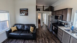 A compact living space with a black leather sofa, a kitchen with modern appliances, and a staircase leading to an upper level. - Moab Tiny Home Near Arches | Sleeps 6 | King + Loft | Mill Creek Falls (Moab)