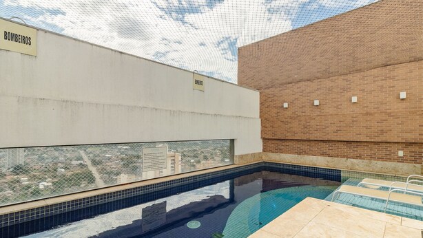 A swimming pool with a view of the city, surrounded by a brick wall and a white ceiling with a mesh pattern. - Apartment Next to Flamboyant Shopping Mall - ESS (Goiânia)